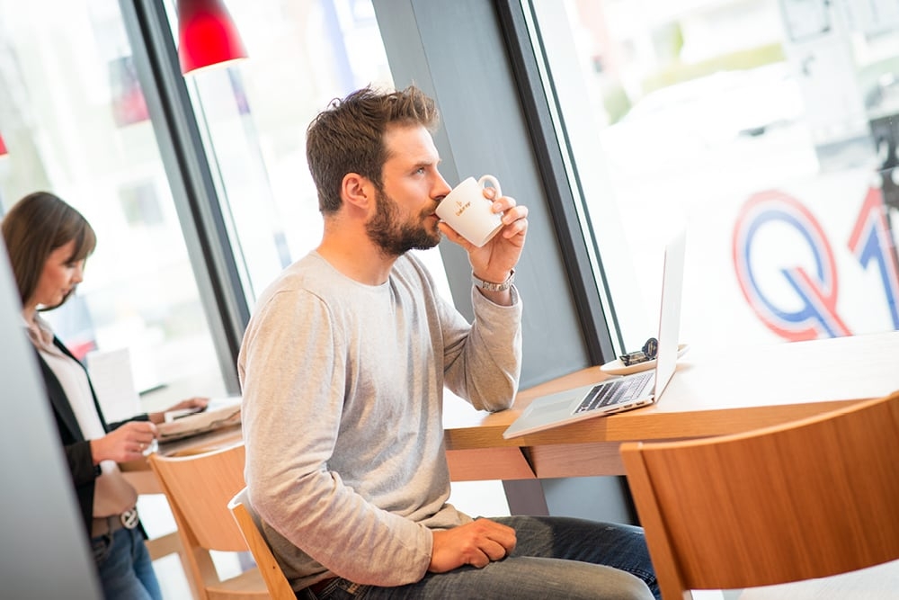 Aufenthaltsqualität an den Q1 Autostrom Ladestationen Mann trinkt Kaffee in Q1 Tankstelle